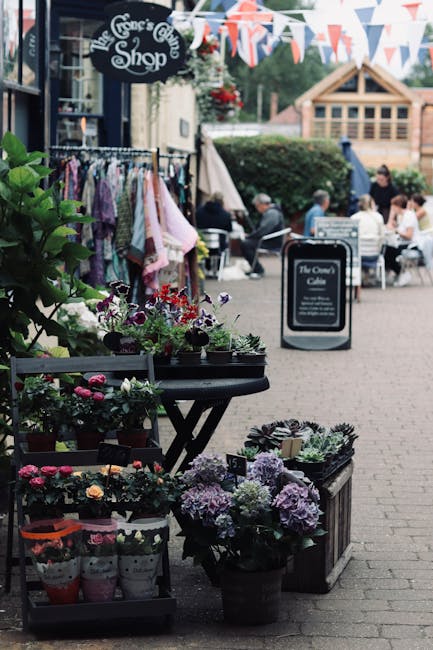 A vibrant display of fresh flowers arranged in black pots and wicker baskets outside The Grace's Cottage Shop, featuring various blooms including hydrangeas in soft purple, pink, and white, complement