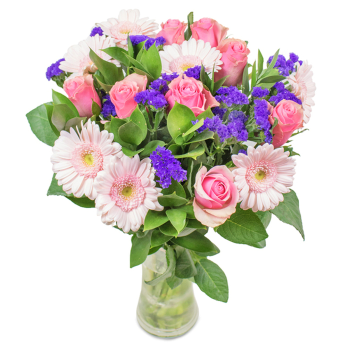 Displayed against a spotless white backdrop in the heart of Colney Hatch, this elegant floral arrangement showcases a perfect harmony of form and colour. Seven to nine pink roses, some tightly furled, others softly opening, highlight the bouquet's core, their petals swirling in exquisite spirals and offering a palette of warm and gentle hues. Nestled alongside, five to seven pale pink gerbera daisies-each with a generous, round face and nearly white center-provide a charming complement, their textured petals radiating outward in subtle waves. Interspersed vivid purple statice introduces playful contrast and intricate texture, echoing the untamed bounty of local wildflower meadows or the lively colours popping up along Colney Hatch Lane. Deep green foliage gathers at the base, abundantly framing the blooms and enhancing the sense of freshness characteristic of just-picked flowers from a local Colney Hatch florist. The arrangement is cradled in a clear glass vase, with water glinting softly and stems on honest display, evoking the feeling of a freshly delivered gift or centerpiece. A bouquet like this feels at home marking special occasions: birthdays, anniversaries, Mother's Day, or simply serving as a joyful accent for near Victoria Park or an office nearby. Through its palette and thoughtful structure, it expresses celebration, affection, and all the natural beauty Colney Hatch has to offer.